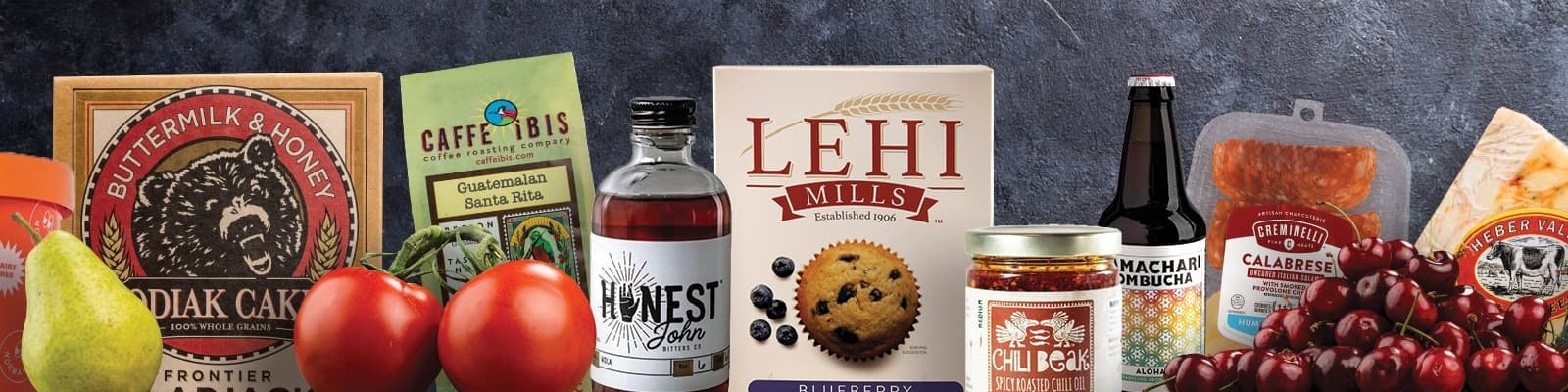 An assortment of local Utah grocery products including Kodiak Cakes, Caffe Ibis coffee, Lehi Mills, Mamachari Kombucha, Creminelli charcuterie, Heber Valley cheese, and fresh produce