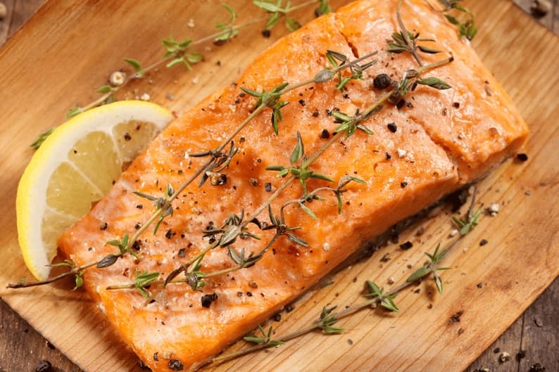 Cooked salmon fillet garnished with lemon and thyme on a wooden board